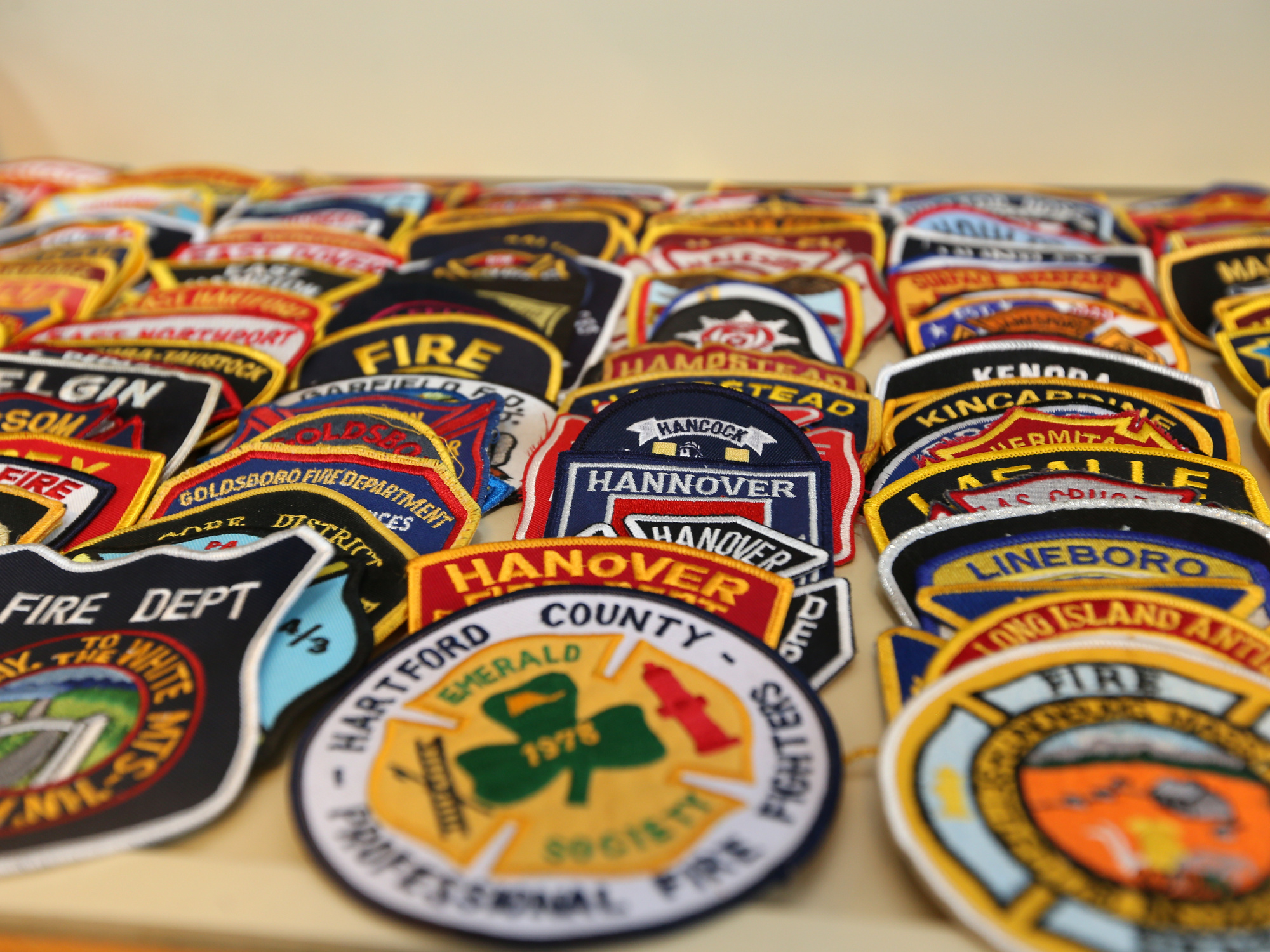 Many fire department patches with different colors and designs are laid out on a surface.